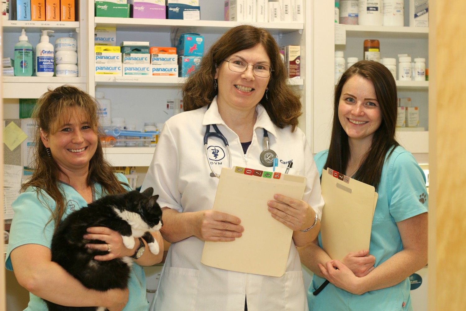 three people in scrubs holding a cat in a pharmacy